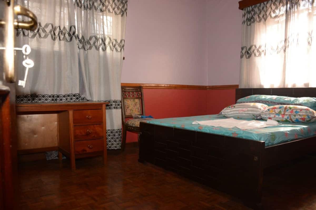 A bedroom with a wooden desk, a bed with colorful bedding, and patterned curtains.