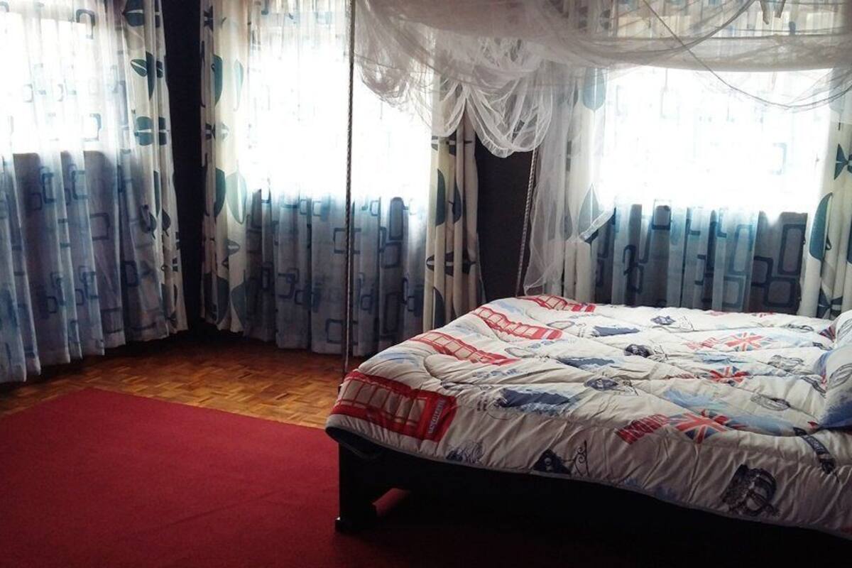 A bedroom with a bed, a red carpet, and curtains with a geometric pattern.