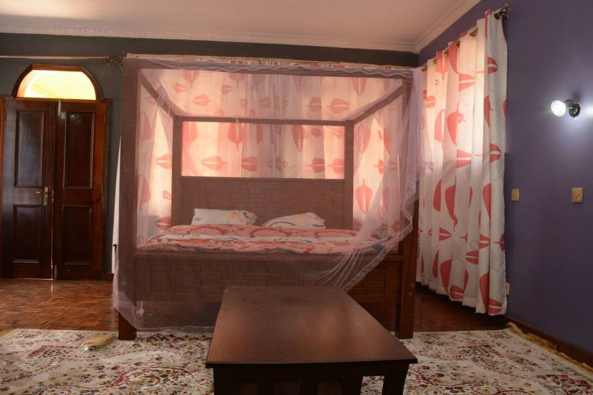 A bedroom with a four-poster bed, a bench, and a patterned rug.