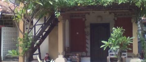 Un patio con suelo de baldosas, plantas en macetas, una escalera y un edificio con techo de tejas.