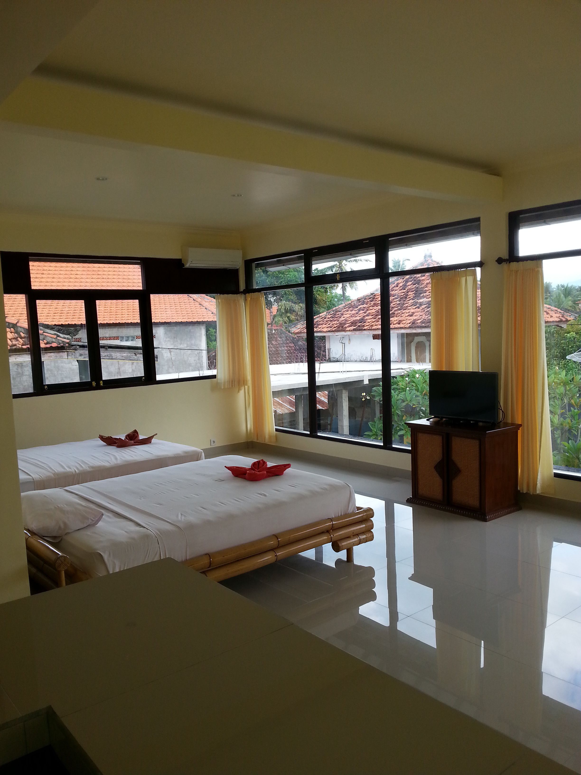 Una habitación de hotel con dos camas, un televisor sobre un mueble de madera y ventanas amplias con cortinas.