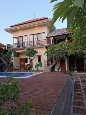 A two-story building with a swimming pool, wooden deck, and tropical plants. - Puri Mandhara Lovina (Buleleng)