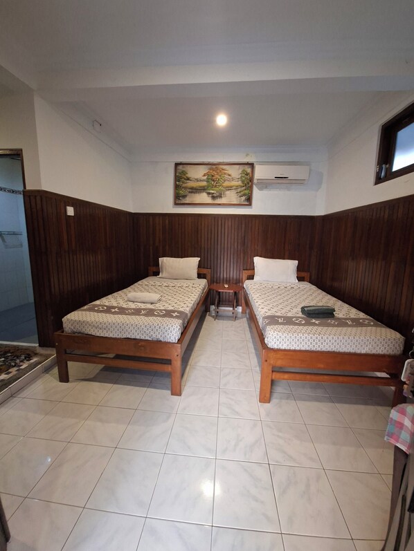 A room with two wooden beds, a small table, and a painting on the wall.