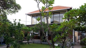 Una casa moderna de dos pisos con techo de tejas, rodeada de un jardín cuidado con varios árboles y un camino pavimentado.