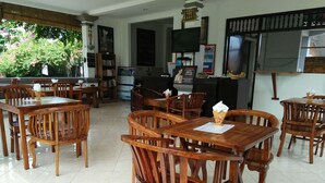Un restaurante con mesas y sillas de madera, un mostrador de recepción, un televisor y una pizarra con el menú.