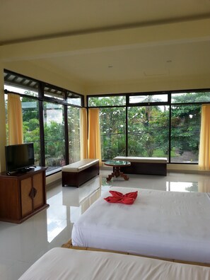 A hotel room with a large bed, a television on a wooden cabinet, a round glass table, and a bench. - Puri Mandhara Lovina (Buleleng)