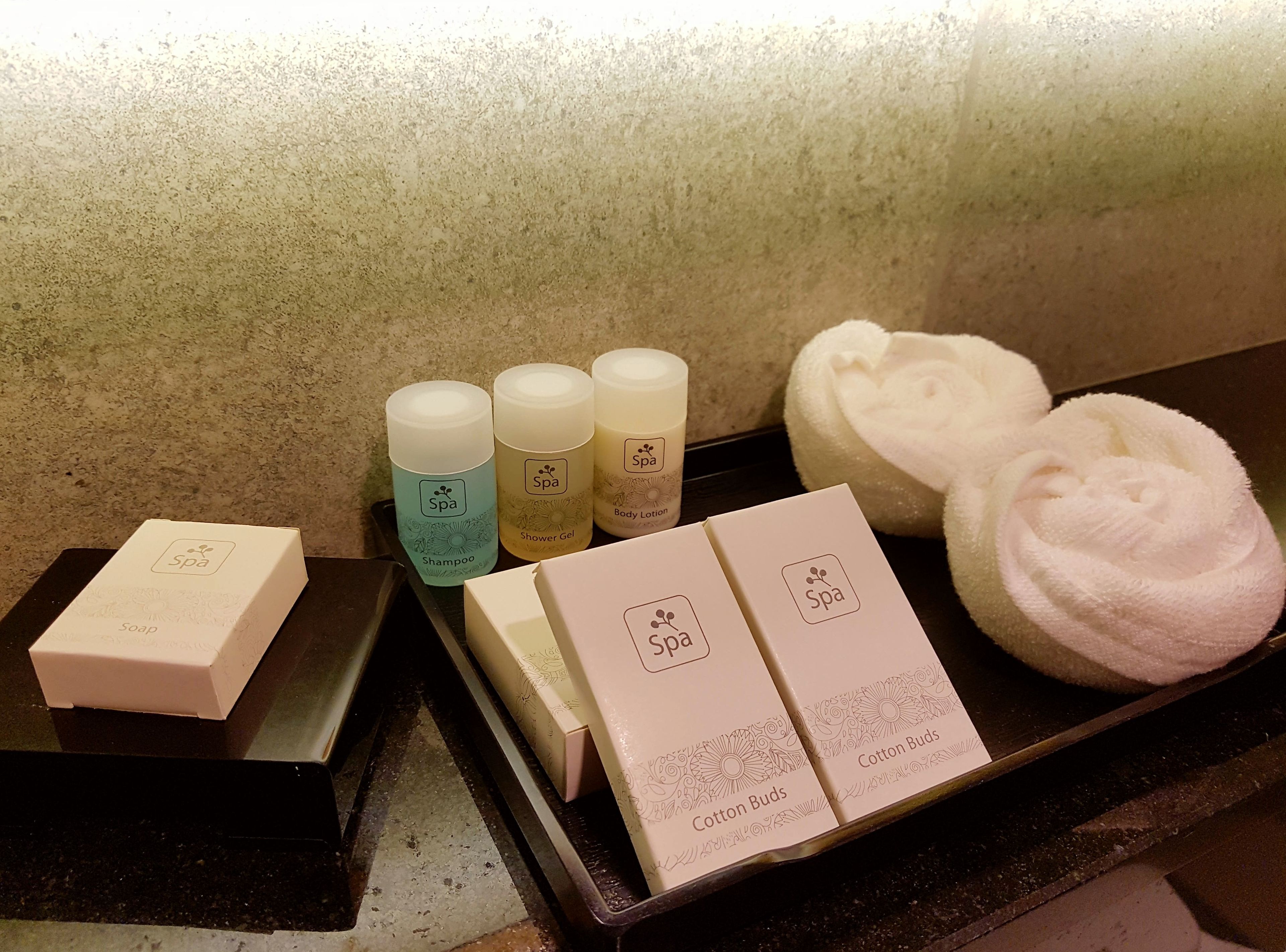 Una bandeja con productos de spa, como champú, gel de ducha, loción corporal, hisopos y jabón.