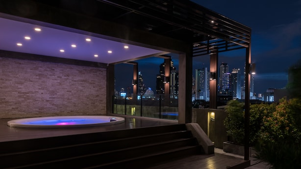 Un área moderna de hidromasaje al aire libre con vistas a un horizonte urbano, escalones que conducen al jacuzzi y una estructura de pérgola.