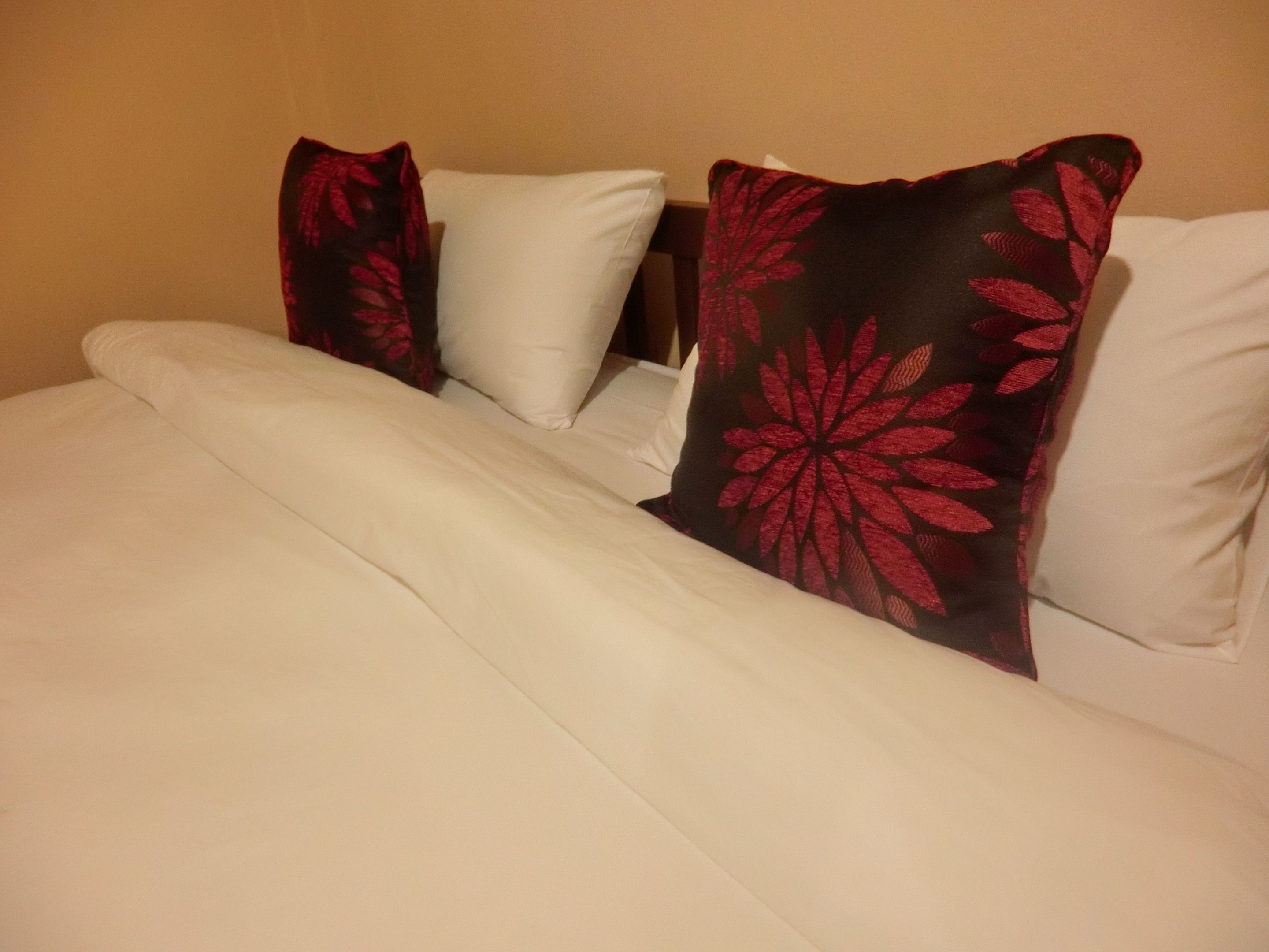 A bed with white bedding and two decorative pillows with red floral patterns.