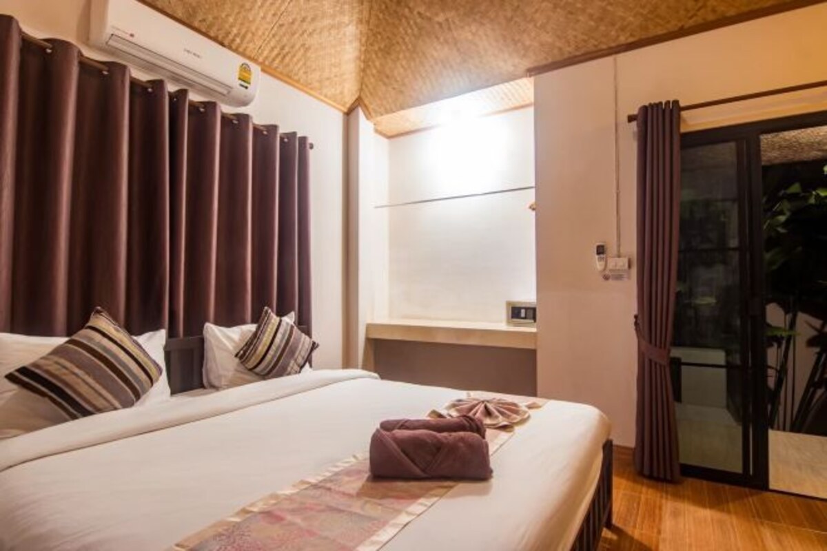 Habitación de hotel con cama, mesita de noche, aire acondicionado instalado en la pared y puerta corrediza de vidrio que da a un balcón.
