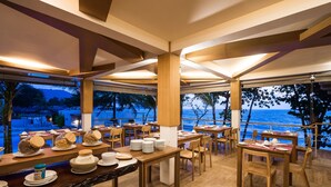 A restaurant with wooden tables and chairs, a view of the ocean, and a beach in the background. - White Sand Samui Resort (Koh Samui)