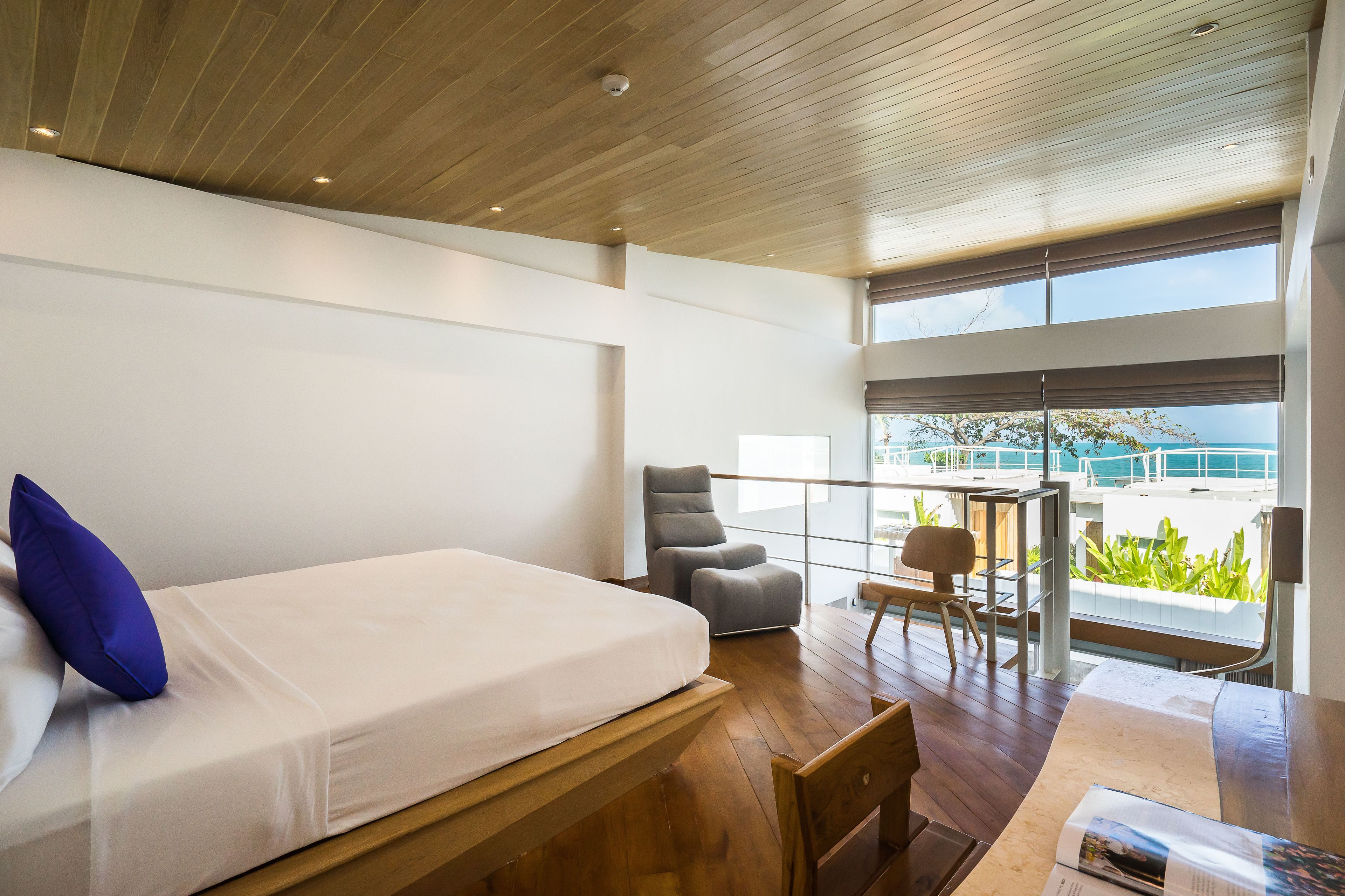 A modern hotel room with a large bed, a seating area with a table, and a balcony with a view of the sea.