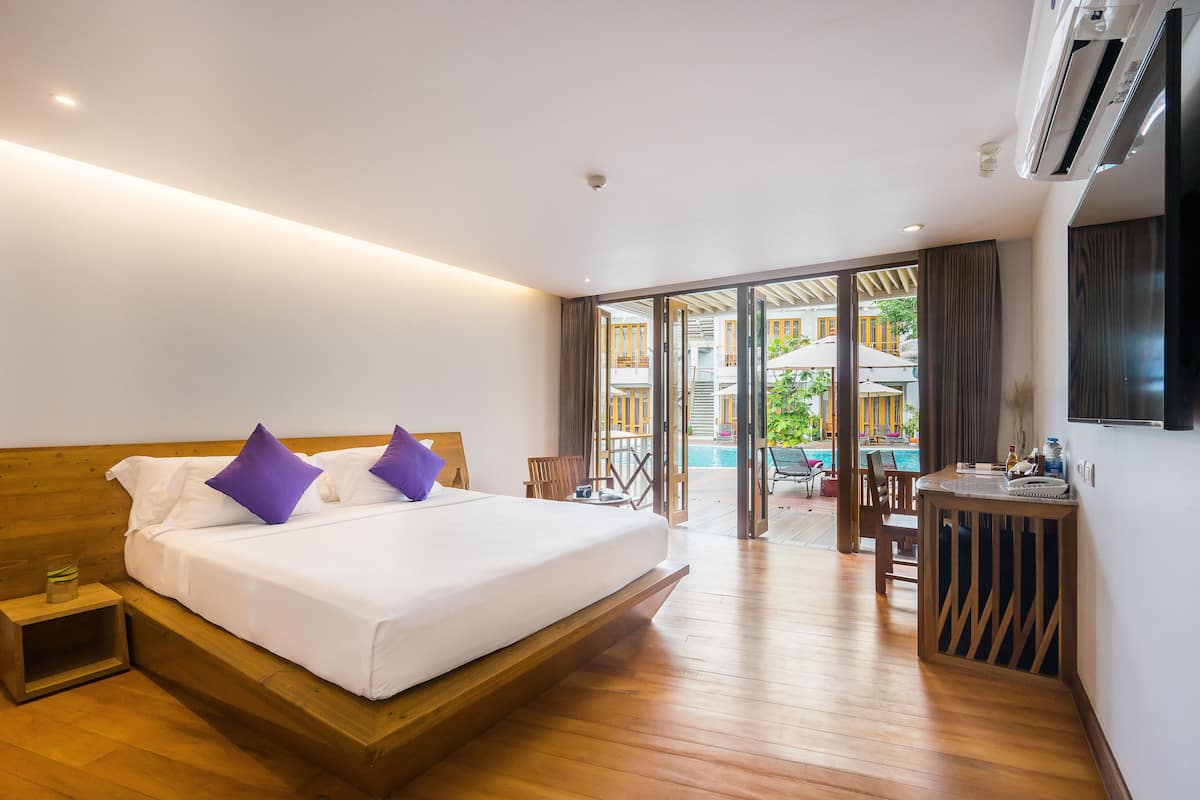 Habitación de hotel con una cama de madera, una mesita de noche pequeña, un televisor y vistas al área de la piscina.