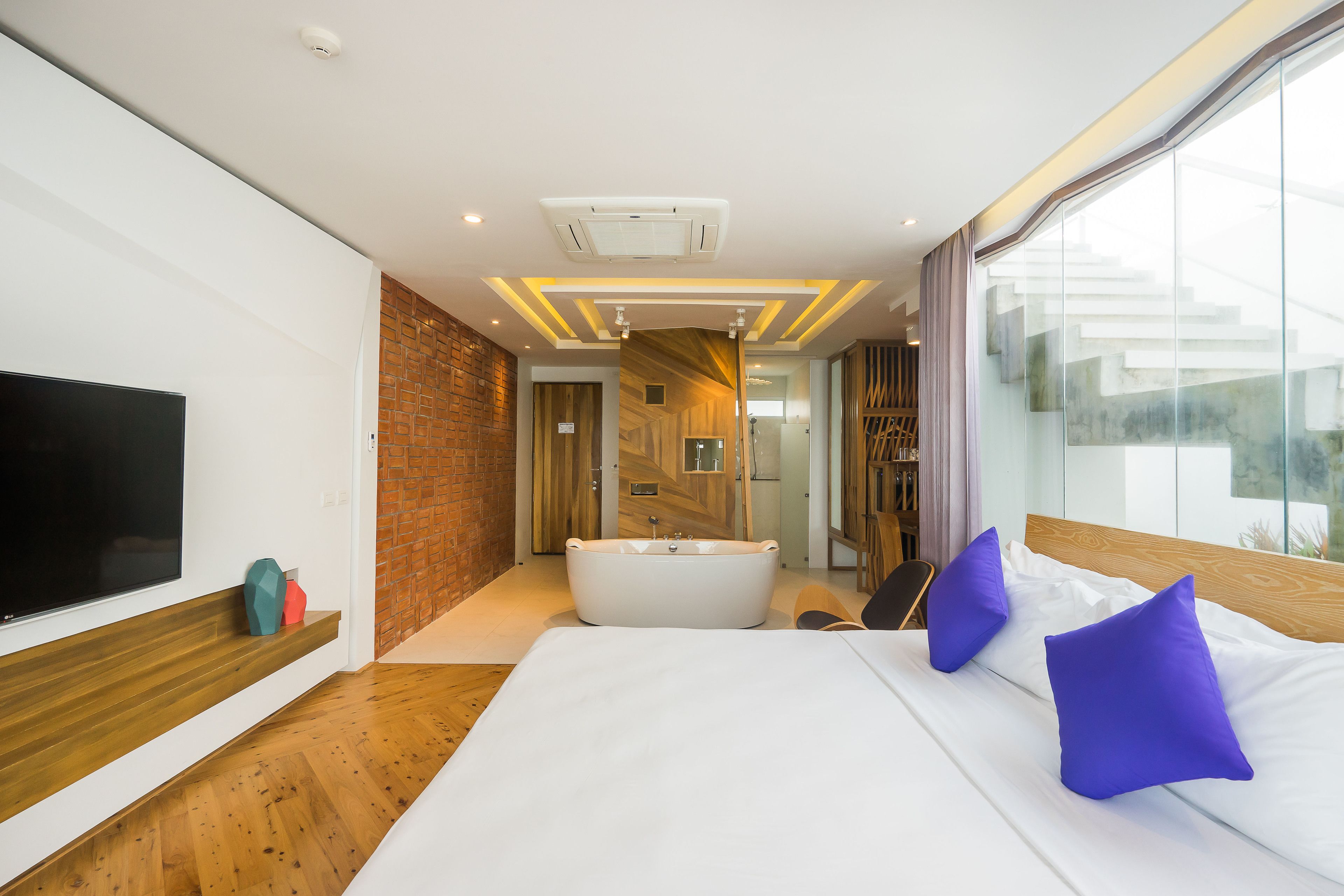 A modern hotel room with a large bed, a flat-screen TV, a bathtub, and a view of the city.