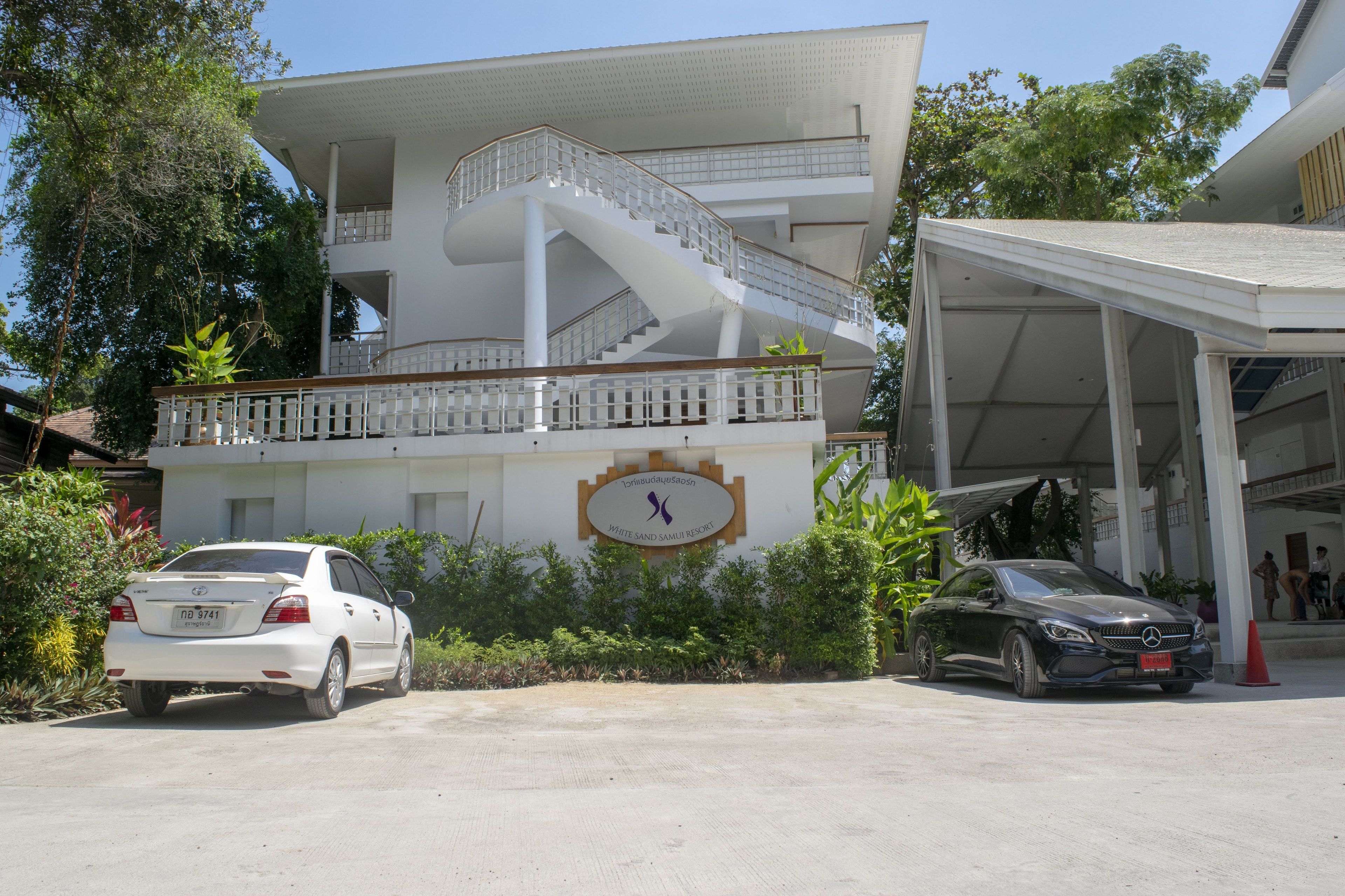 A modern building with a white facade, a curved staircase, and a covered parking area.
