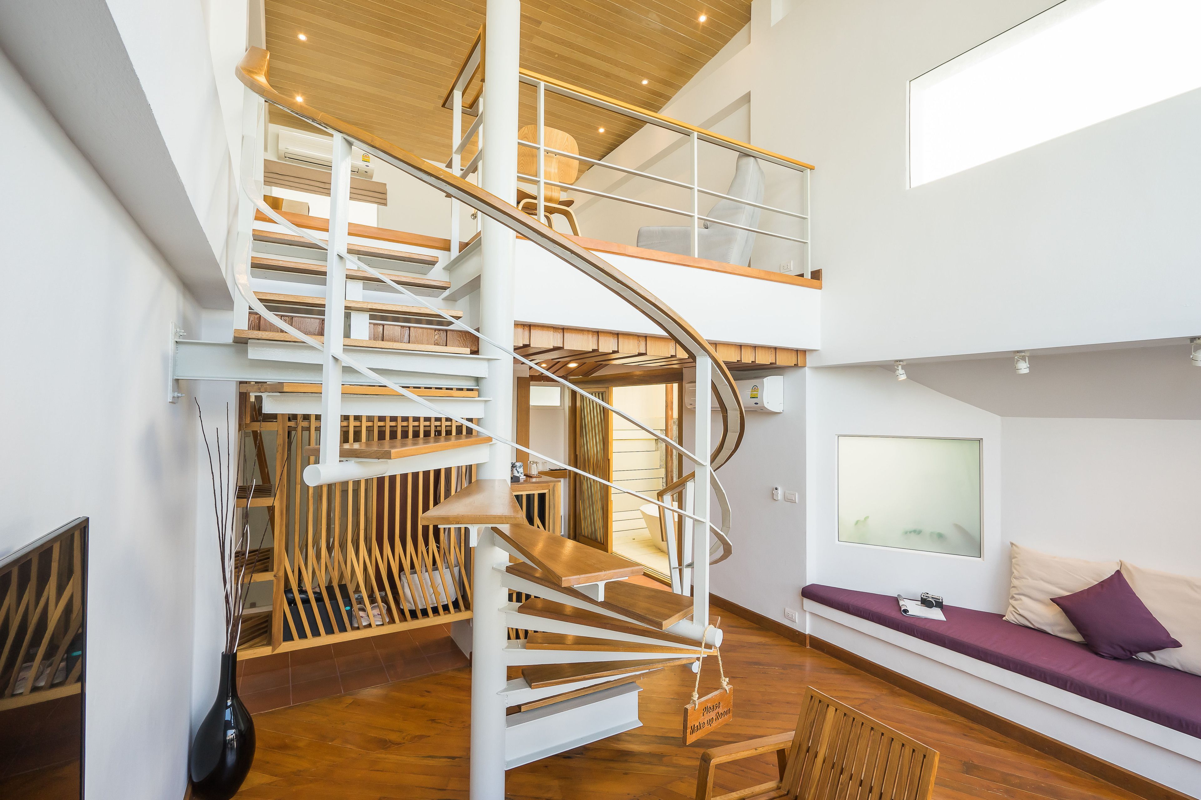 A modern interior with a spiral staircase, a seating area with cushions, and a large window providing natural light.