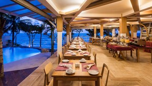 A long dining table with chairs, set for a meal, overlooking a pool and the ocean. - White Sand Samui Resort (Koh Samui)