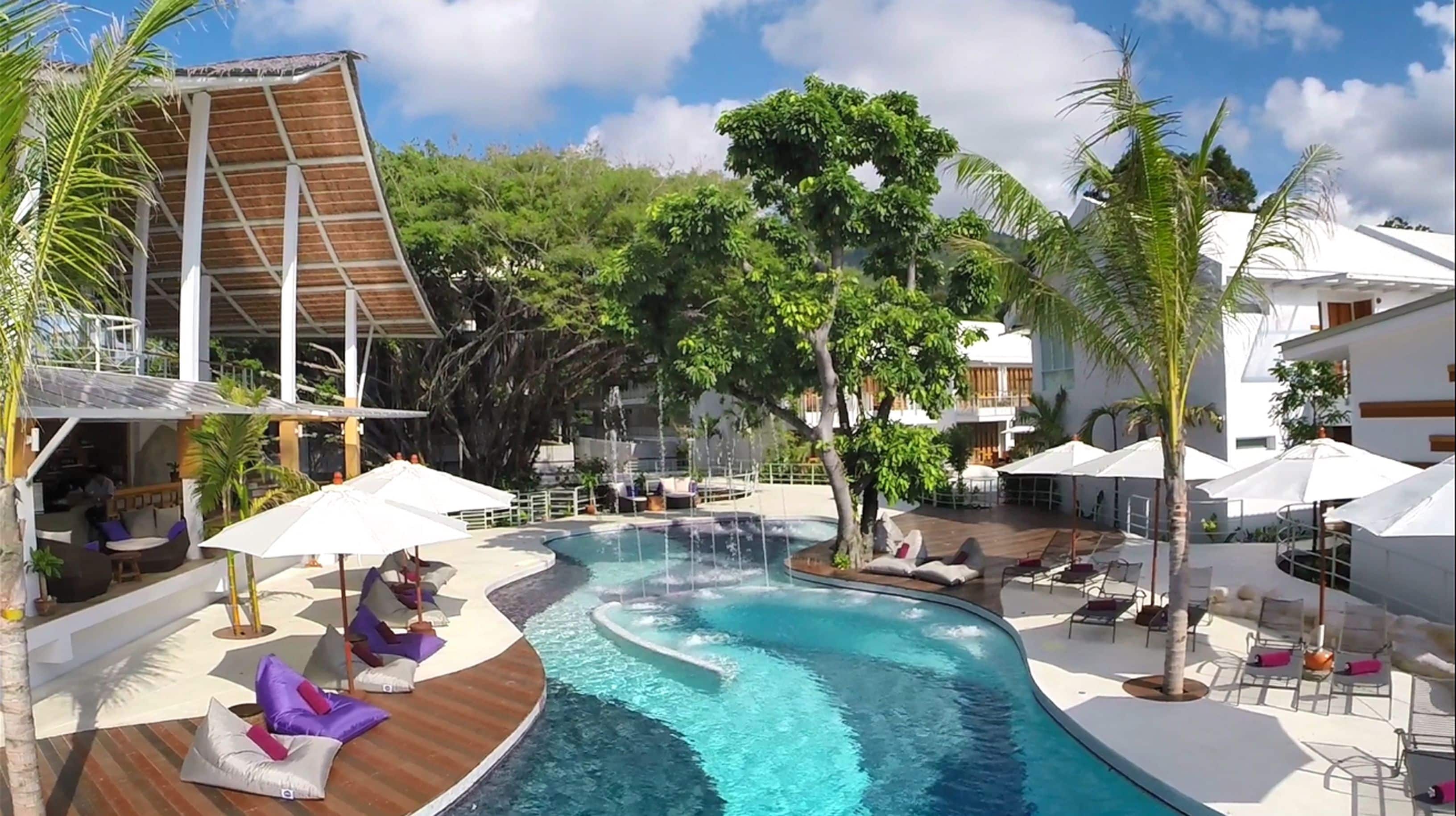 Een zwembadgedeelte van een resort met ligbedden, parasols en een houten terras.
