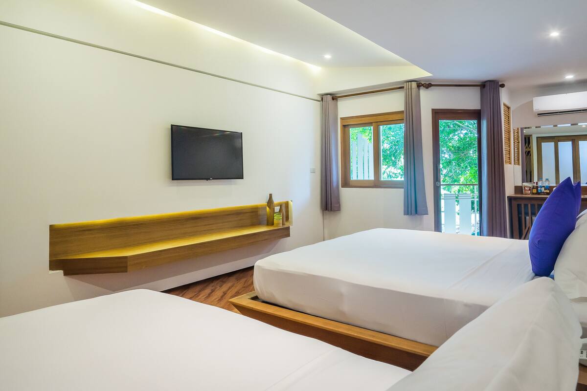 Habitación de hotel con dos camas, un televisor montado y una ventana con cortinas.