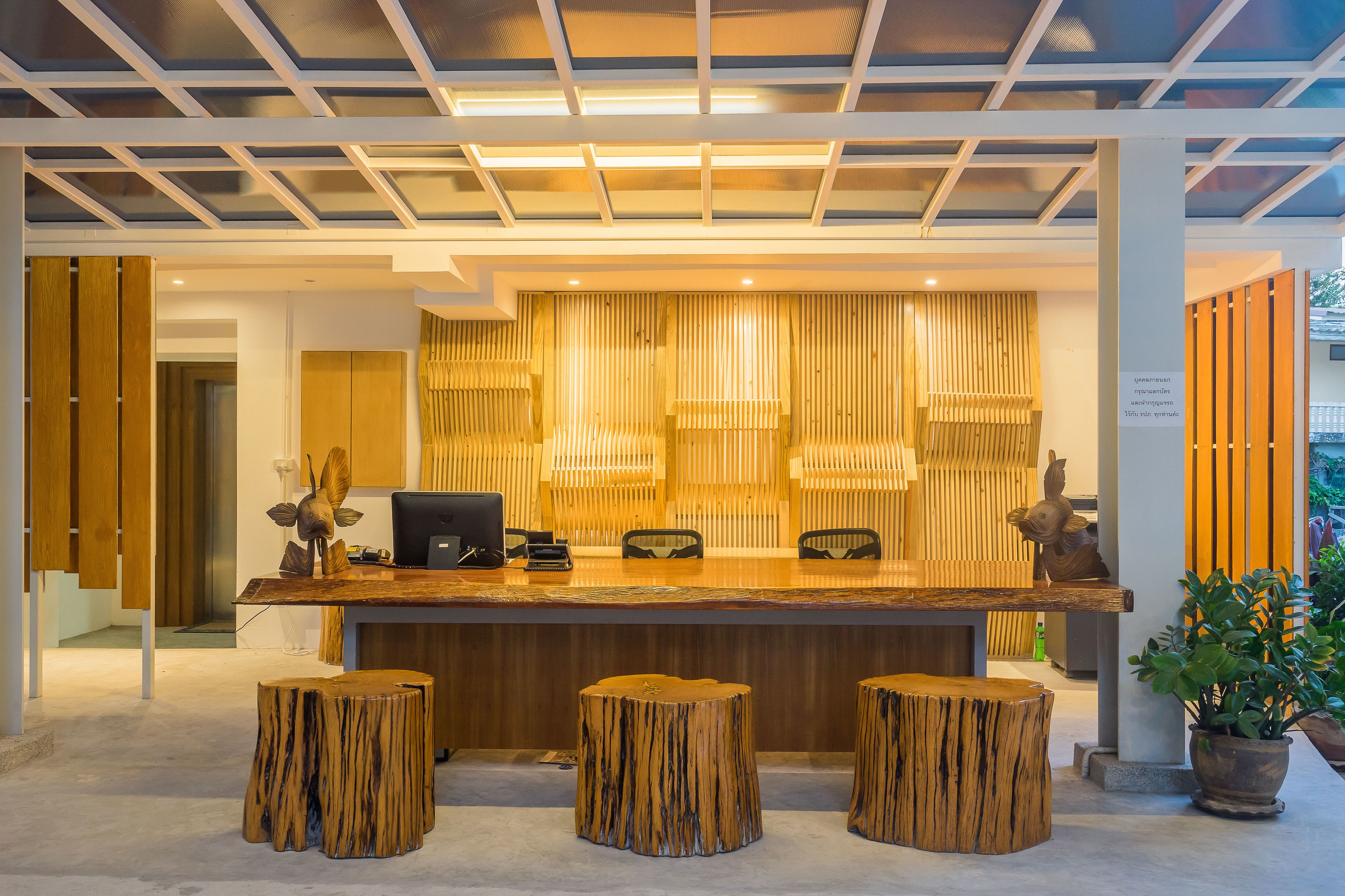 A reception area with a wooden reception desk, three wooden stools, a computer, and a decorative wall panel.