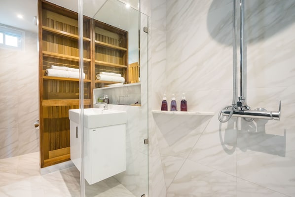 Une salle de bain moderne dotée d’une douche à l’italienne avec des parois en verre, d’un meuble-lavabo en bois avec un miroir et d’une étagère pour les articles de toilette.