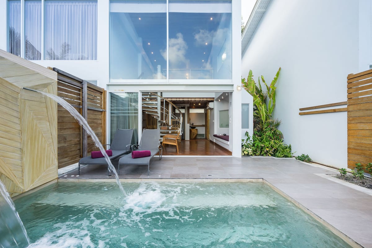 Una piscina interior moderna con pared de vidrio, terraza de madera y zona de estar.