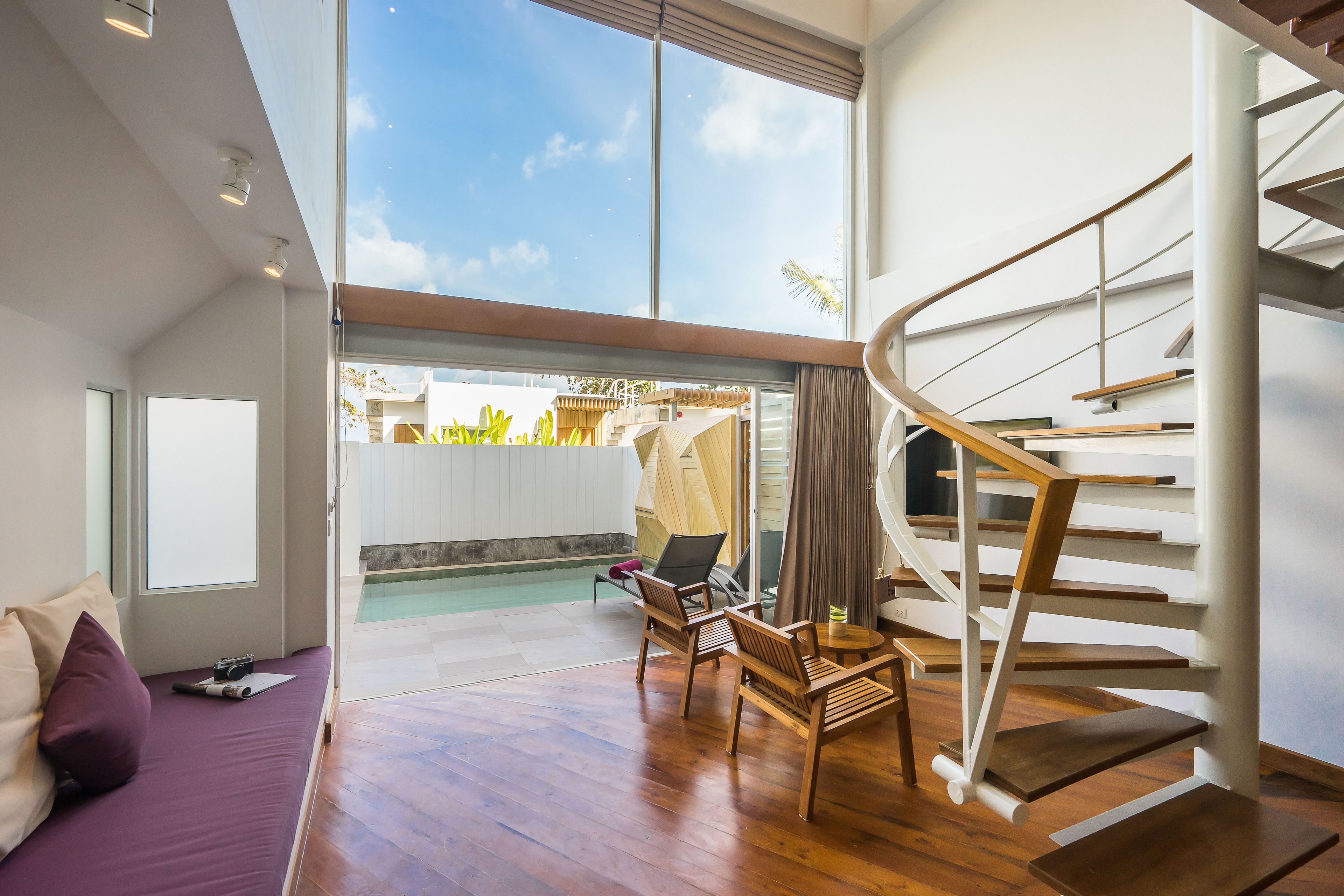 A modern interior with a wooden staircase, a pool area visible through glass doors, and a seating area with a sofa and chairs.