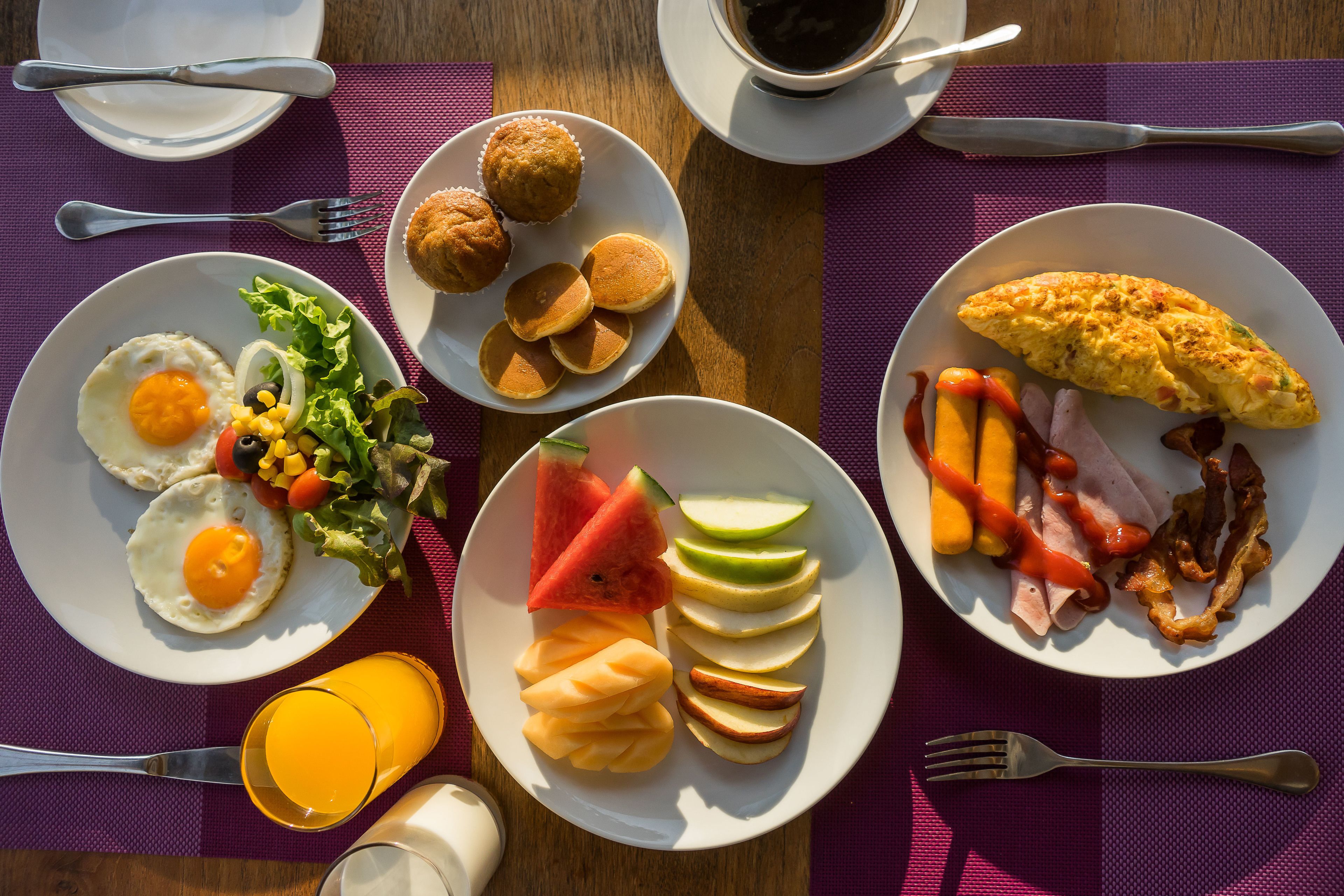 Une table de petit-déjeuner avec des assiettes d’œufs, de crêpes, de bacon et des fruits.