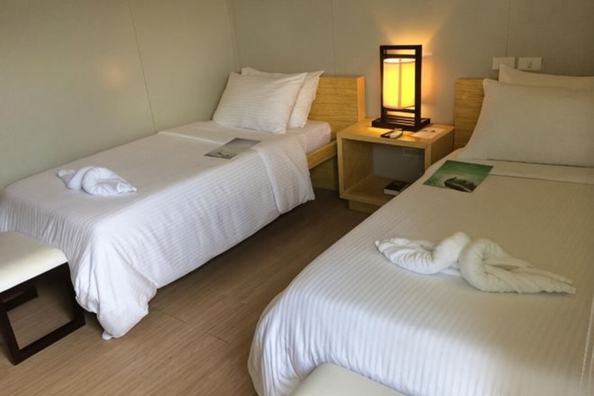 A hotel room with two single beds, a bedside table with a lamp, a small desk, and a bench.