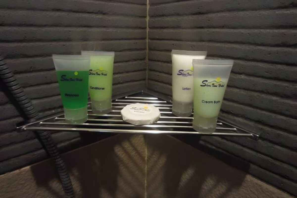 Un estante con diversos artículos de aseo personal, incluyendo una botella de champú verde, una loción, una crema de baño y una pastilla de jabón.