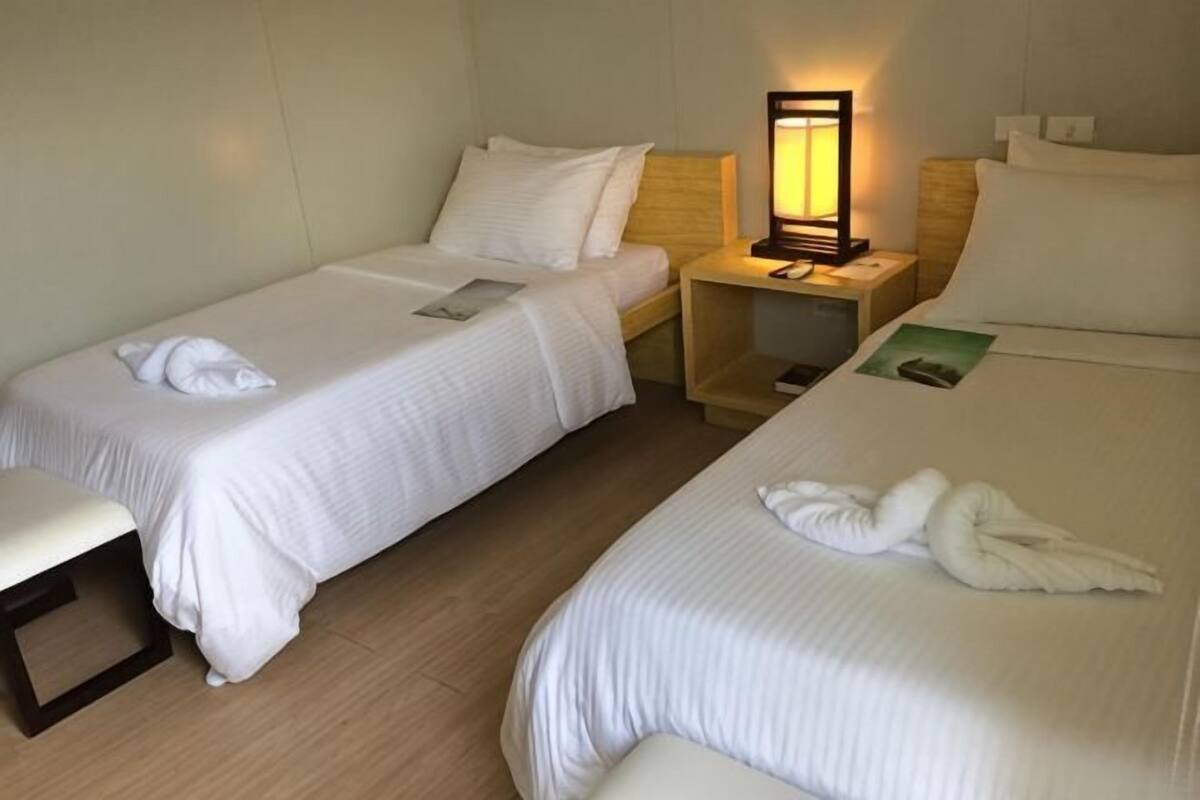A hotel room with two single beds, a bedside table with a lamp, a small desk, and a bench.