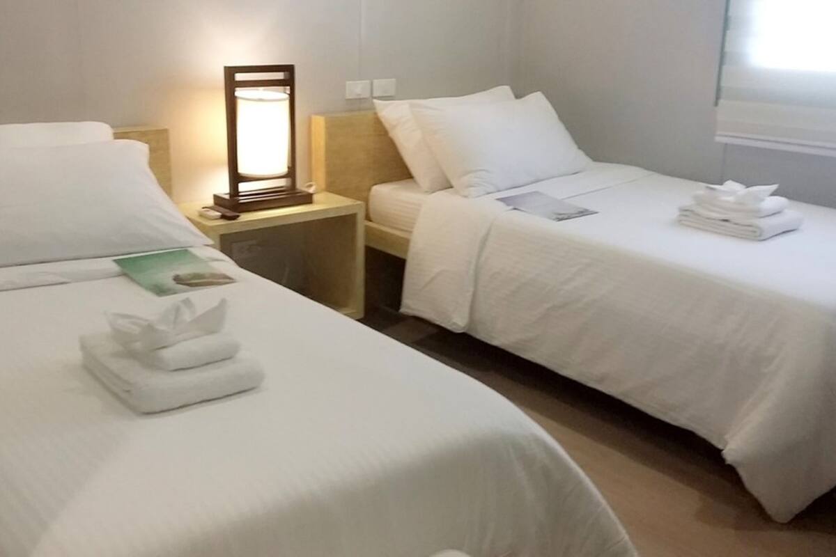 Hotellihuone, jossa on kaksi erillistä sänkyä. Jokaisessa sängyssä on valkoiset lakanat ja siististi taitettu pyyhe. Sänkyjen välissä on yöpöytä, jossa on lamppu.