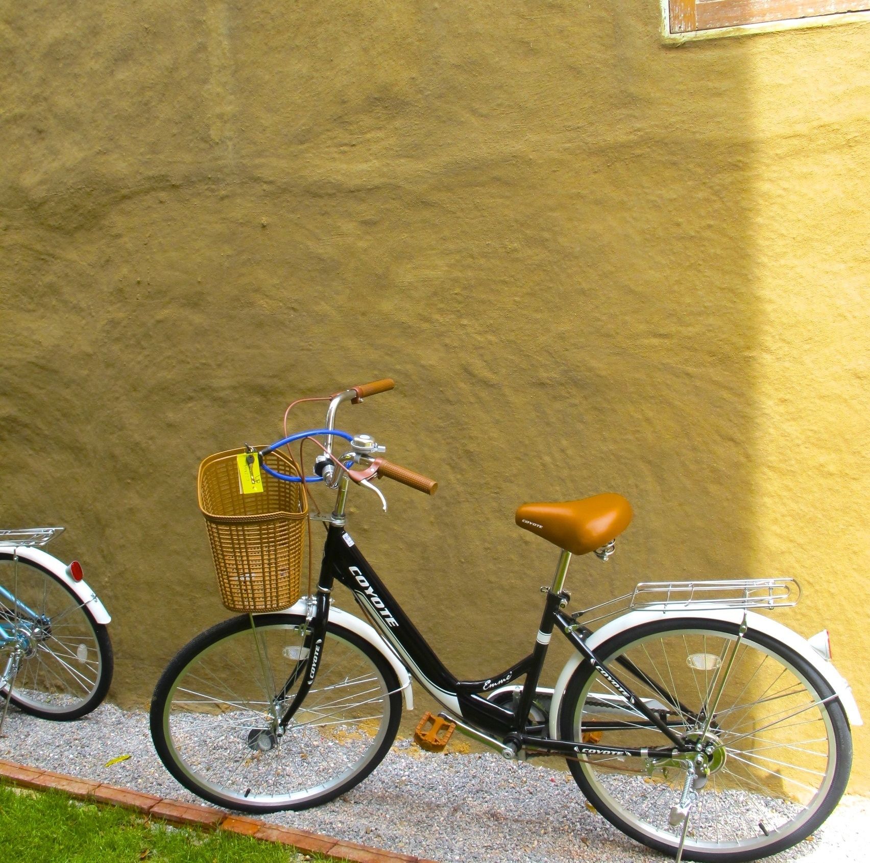 A stationary bicycle with a basket and a seat, parked against a textured wall.