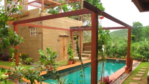 A pool area with a wooden pergola, a small building with a door, and various potted plants around the pool. - Pranberry Earth (Pranburi)