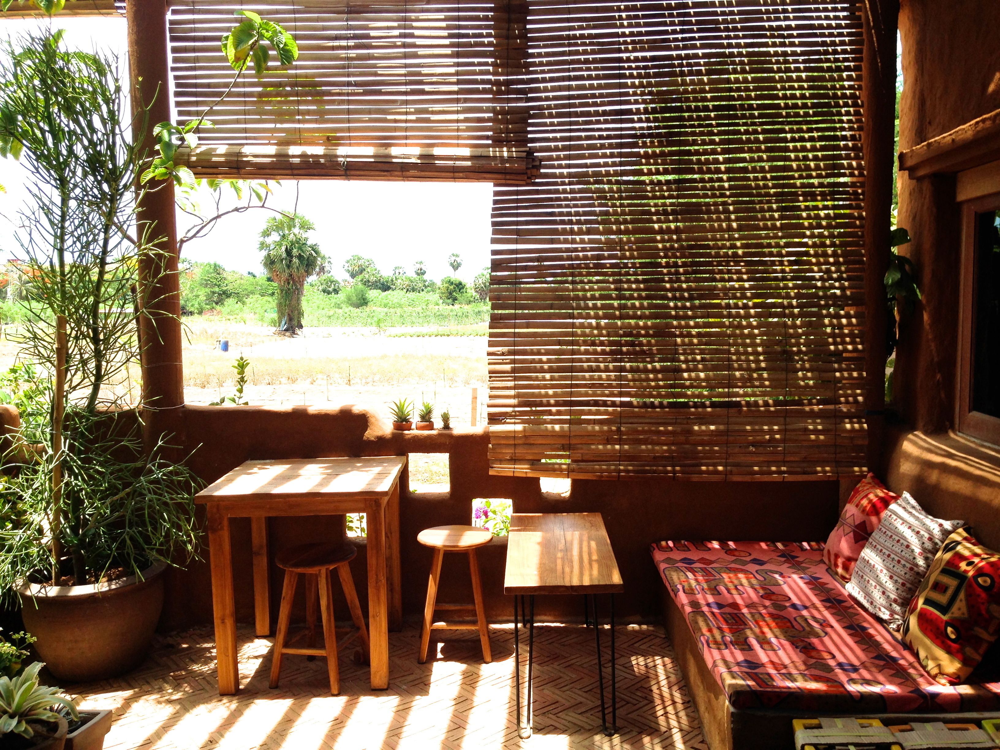 A room with a wooden table, two stools, a small table, and a sofa with patterned cushions.