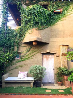 A courtyard with a stone bench, a wooden door, and potted plants. - Pranberry Earth (Pranburi)