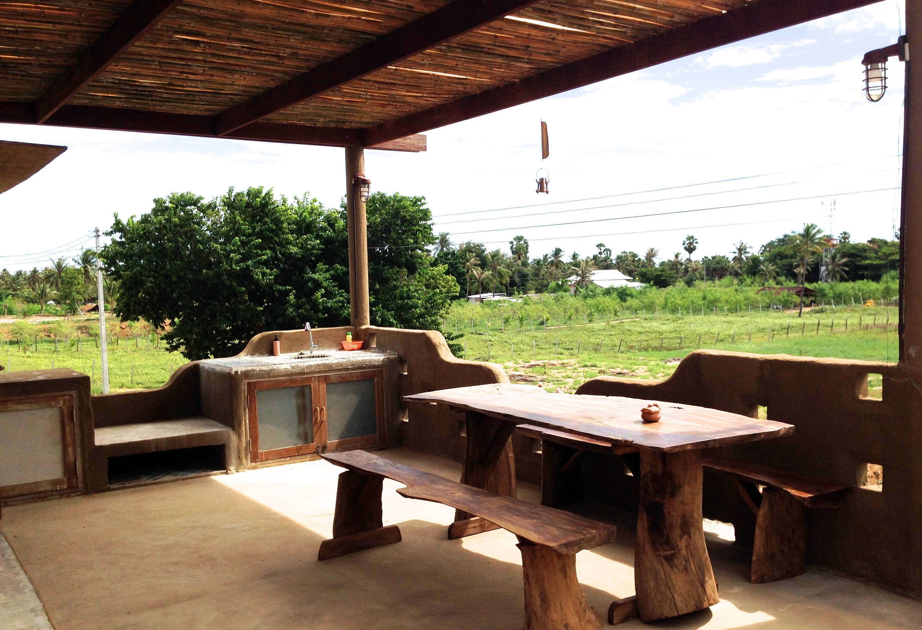 An outdoor patio with rustic wooden furniture, including a table and benches, under a wooden roof.