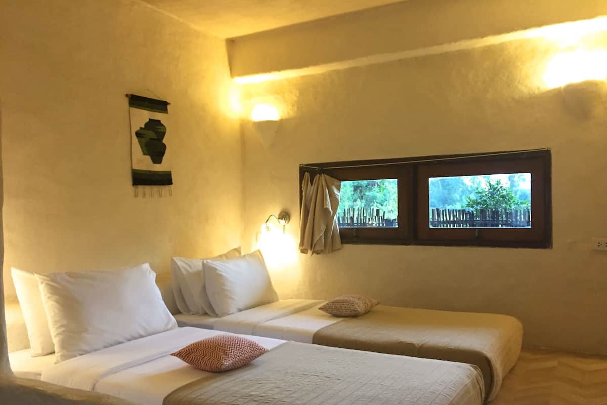 A room with two beds, a window with a view of greenery, and a wall-mounted light fixture.