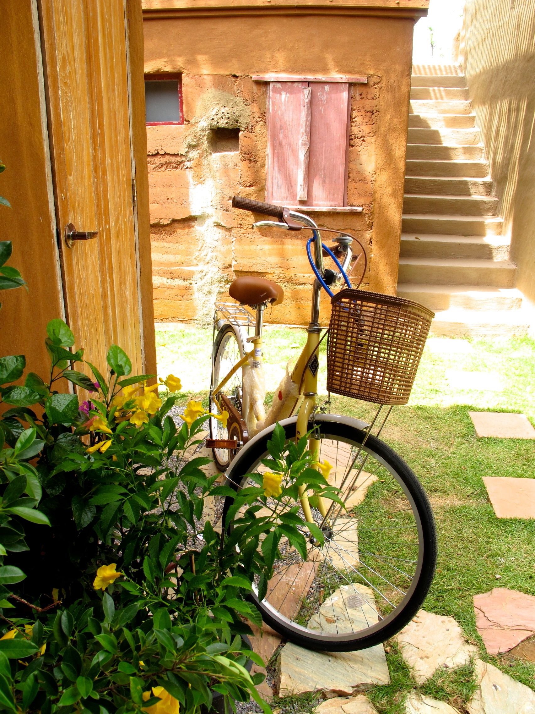Uma bicicleta estacionada em frente a um edifício rústico com porta de madeira e janela com persiana vermelha.