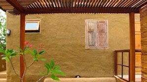 A covered outdoor seating area with a wooden pergola, a small window, and a wall-mounted shutter. - Pranberry Earth (Pranburi)