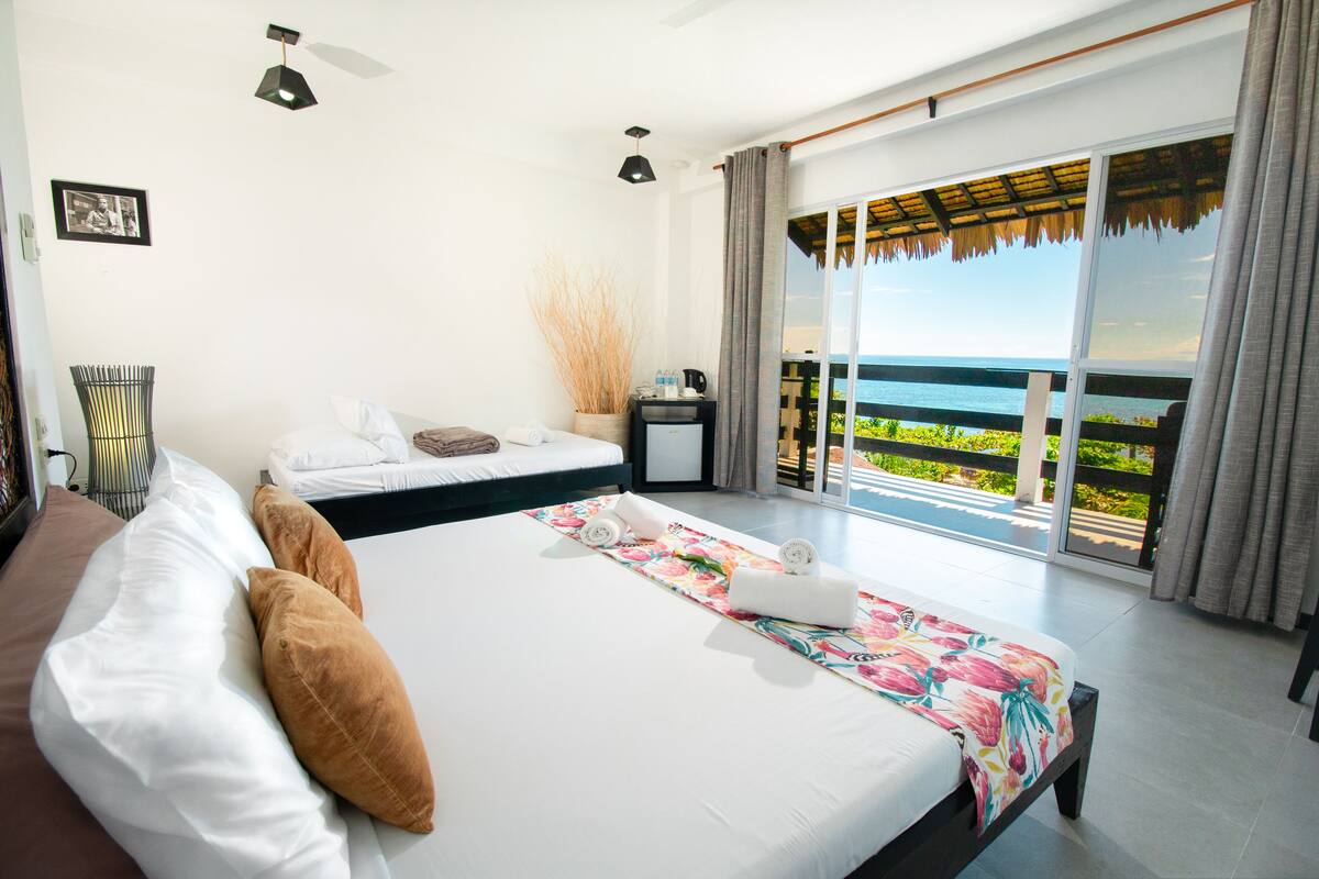 Una habitación de hotel moderna con una cama grande, un escritorio pequeño y un balcón con vista al mar.