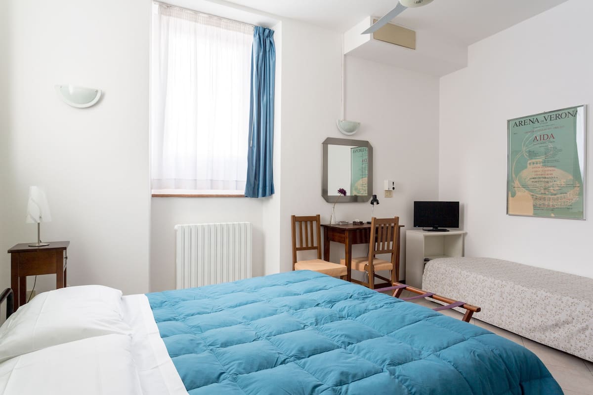 Ein Schlafzimmer mit einem Bett, einem Schreibtisch, einem Stuhl, einem Fernseher und einem Bild an der Wand.