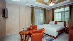 Une chambre d’hôtel avec un grand lit, deux chaises, une petite table avec des bouteilles d’eau et un téléviseur fixé au mur.