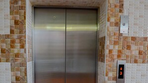 Un ascenseur doté d’un écran numérique affichant le chiffre 3 et d’une lumière rouge, le tout entouré de murs recouverts de mosaïques.