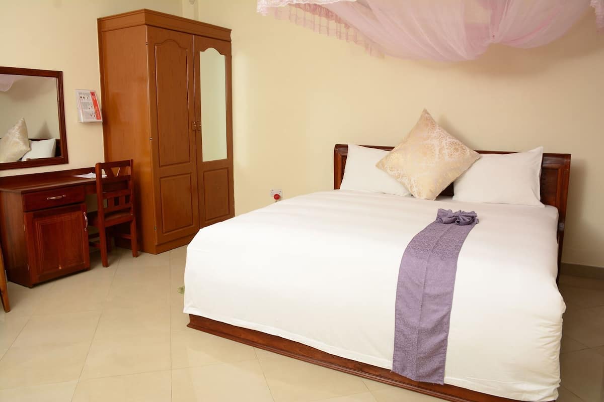 A bedroom with a bed, a wooden wardrobe, a desk, and a chair.