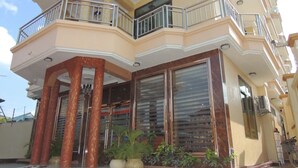 Un immeuble à plusieurs étages, doté d’un balcon au deuxième étage, de grandes portes vitrées et de plantes en pot devant l’entrée.