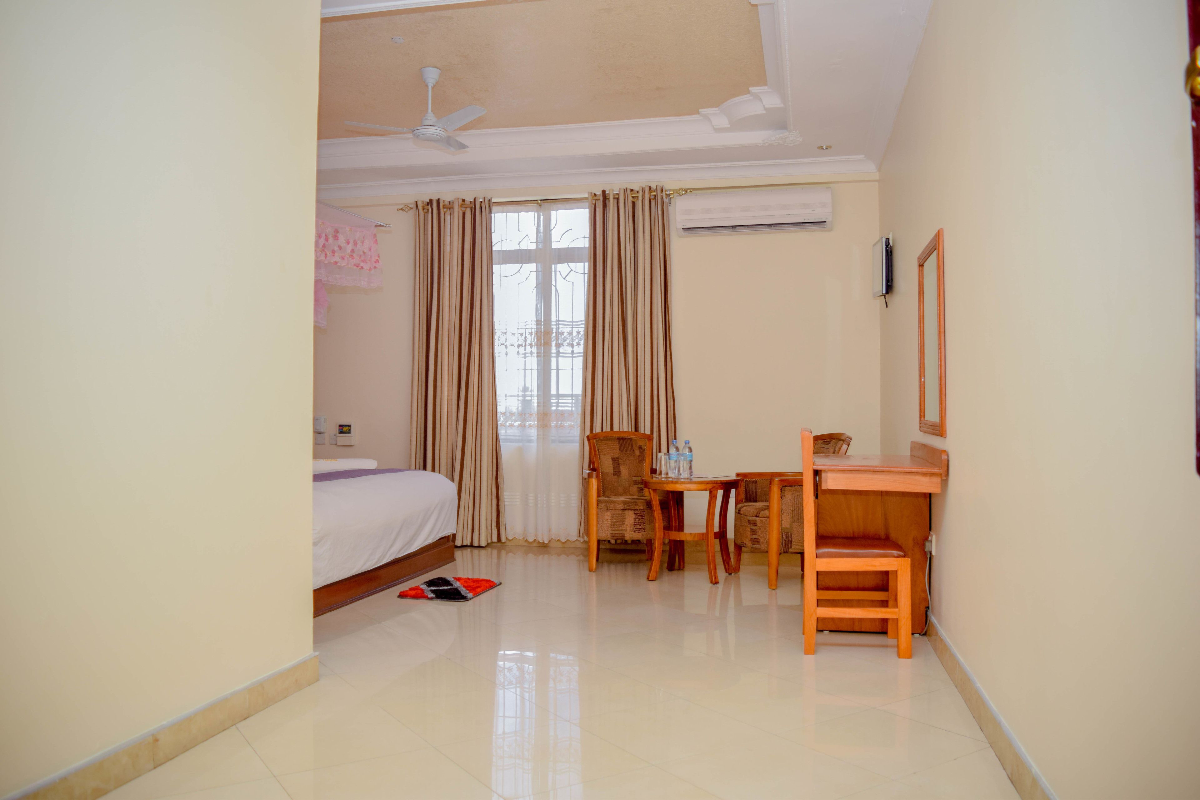 A hotel room with a bed, a desk, two chairs, a ceiling fan, and a window with curtains.