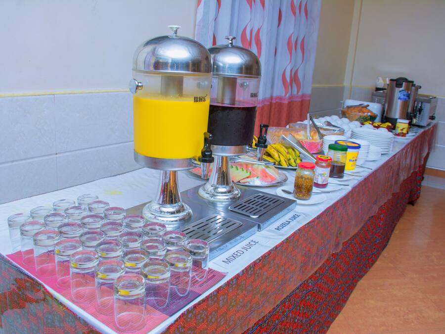 A buffet table with a juice dispenser, a variety of food items, and a patterned tablecloth.
