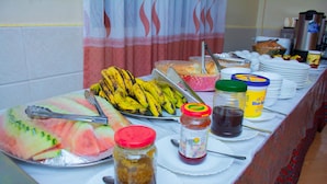 Une table de buffet proposant divers aliments, notamment des tranches de pastèque, des bananes et différentes sauces.