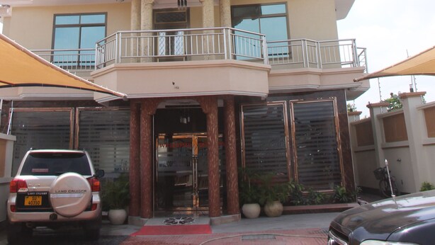 Un hôtel à plusieurs étages doté de balcons, une enseigne bien visible indiquant « SILVER PARADISE LTD. », et un Land Cruiser garé devant.
